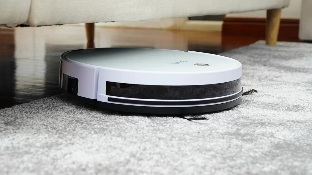 Halı üzerinde koltuk altına giren beyaz bir robot süpürge