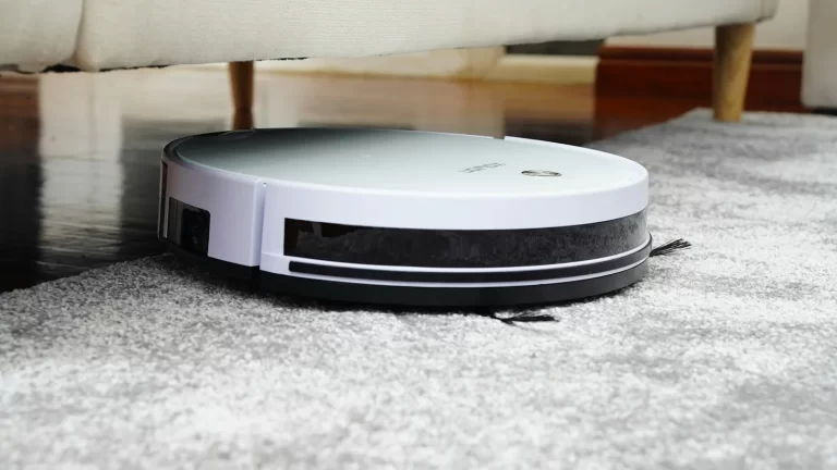 Halı üzerinde koltuk altına giren beyaz bir robot süpürge